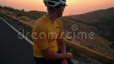 骑自行车的人穿着黄色的t恤在山上看日落。 健身后休息，钢铁侠
